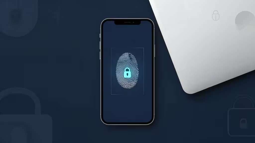 A smartphone displaying a glowing fingerprint icon rests beside a laptop, symbolizing secure biometric authentication.