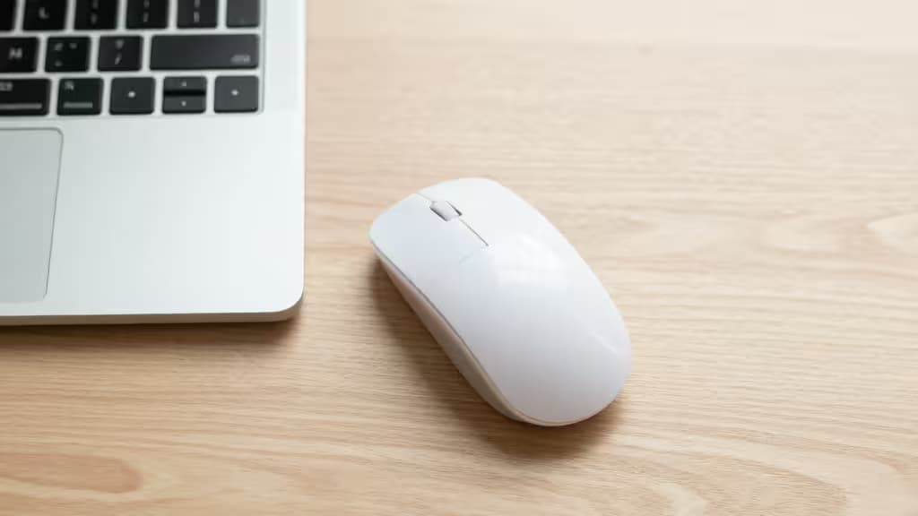 Белая вертикальная эргономичная мышь рядом с серебристым MacBook на светлом деревянном столе