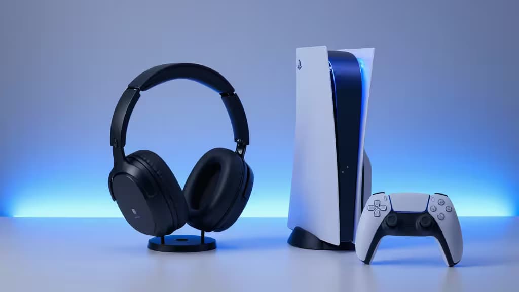 Black over-ear headset stands beside white PS5 console and DualSense controller on minimalist surface.
