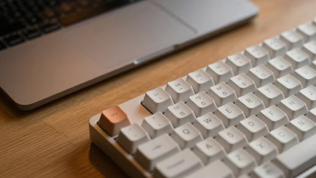 Clavier mécanique blanc avec touche cuivrée posé à côté d'un MacBook argenté sur un bureau en bois.