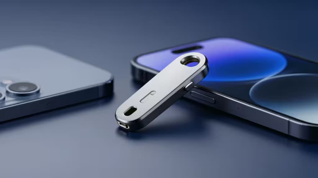 Серебристый металлический FIDO2-ключ безопасности лежит по диагонали на тёмно-синем смартфоне, на заднем плане виден ещё один телефон.