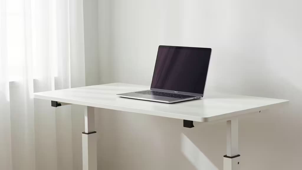 White standing desk riser with laptop sits on small white desk in bright apartment.