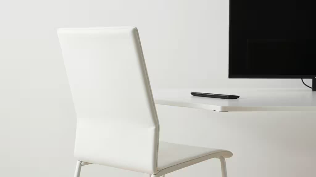 Een witte bureaustoel staat voor een bureau met een monitorarm die een zwart scherm boven het bureau vasthoudt, moderne werkplek met zachte verlichting
