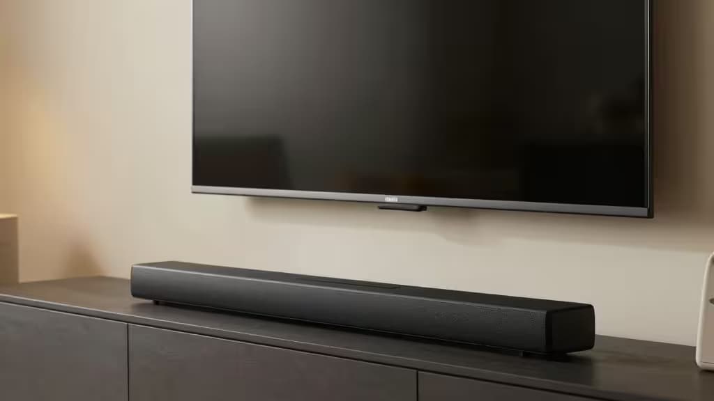 Barre de son moderne posée sur un meuble TV sous un écran plat mural dans un salon minimaliste, éclairage ambiant chaleureux