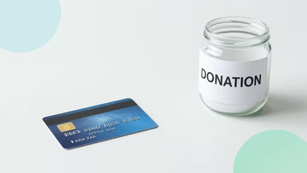 Eine blaue Kreditkarte liegt neben einem Glas mit der Aufschrift „DONATION" auf einer weißen Oberfläche mit sanften blauen und grünen Kreisen.