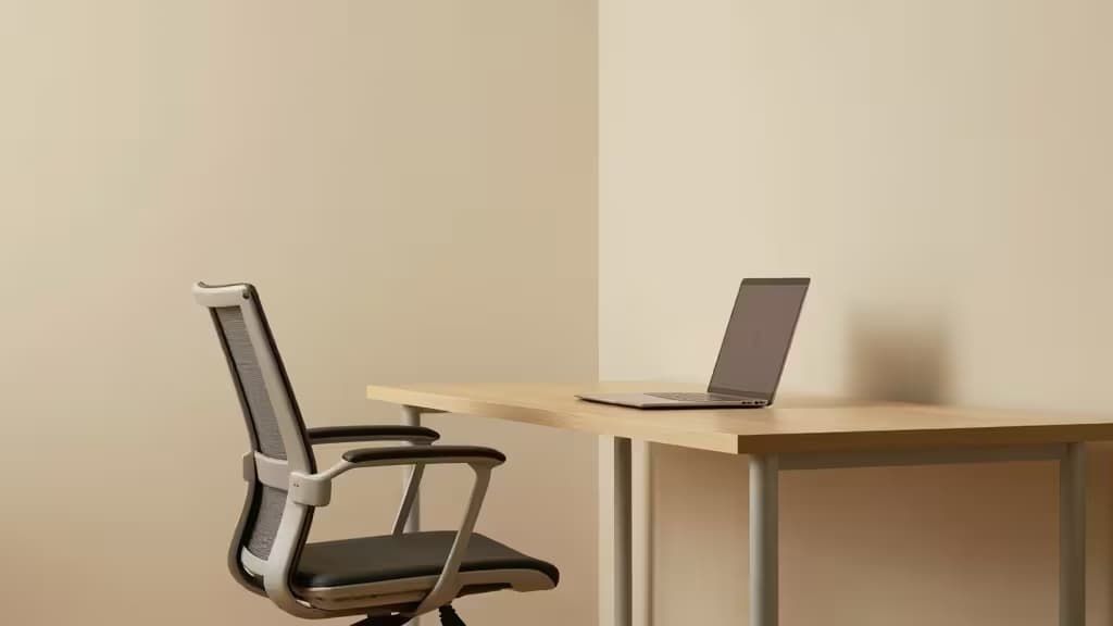A mesh-back ergonomic chair sits beside a minimalist desk with a laptop, showcasing clean lines and neutral tones.