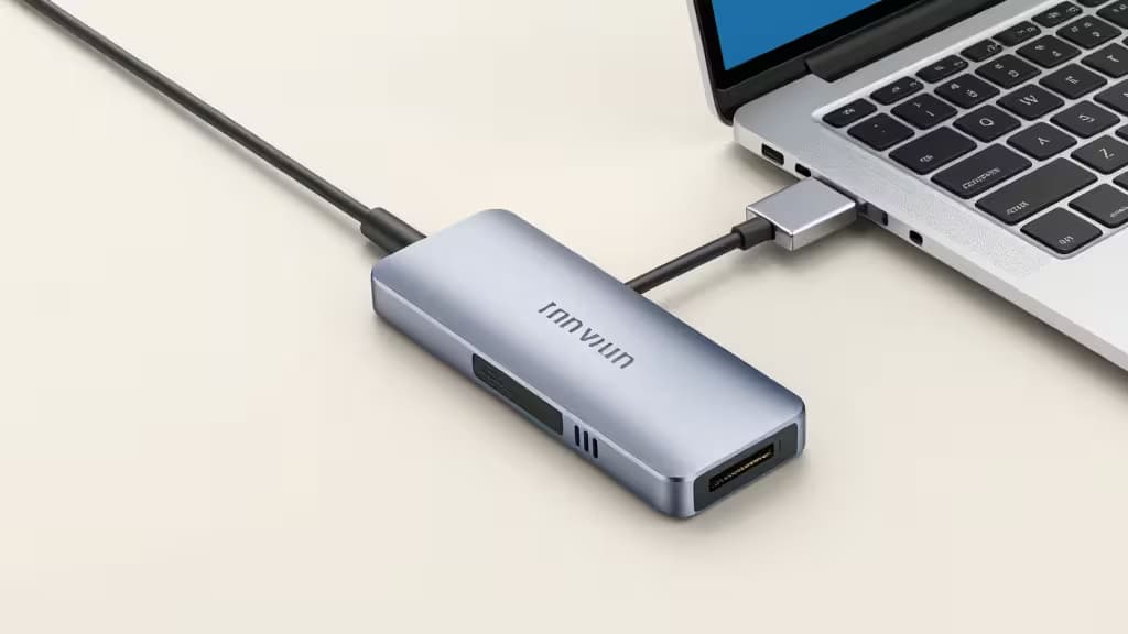 Silver Innviun USB-C hub connects to laptop, displaying HDMI, Ethernet, and SD card ports on its metallic casing.