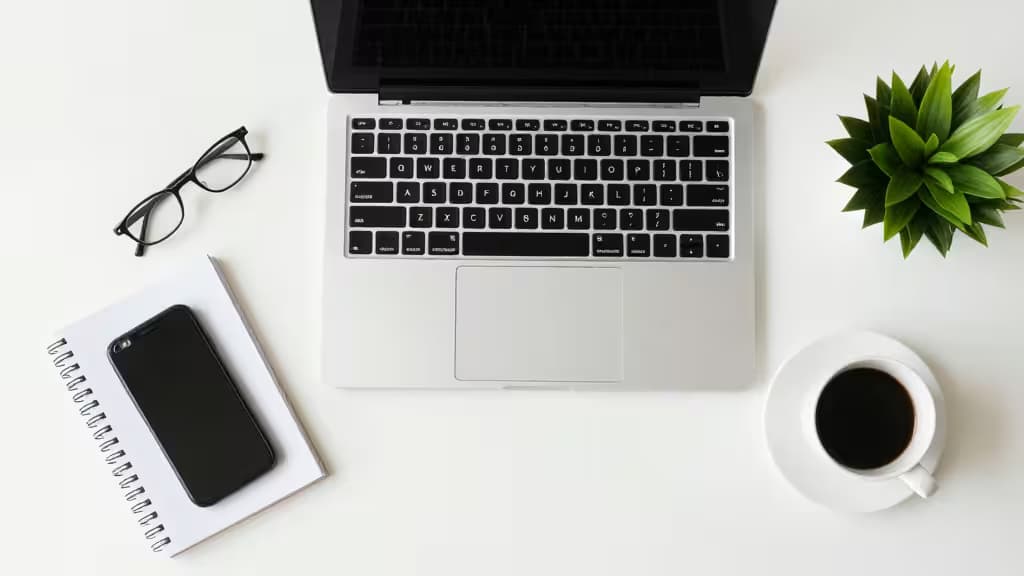 Minimalistyczne biurko freelancera z laptopem, notesem, filiżanką kawy i małą rośliną w miękkim świetle naturalnym