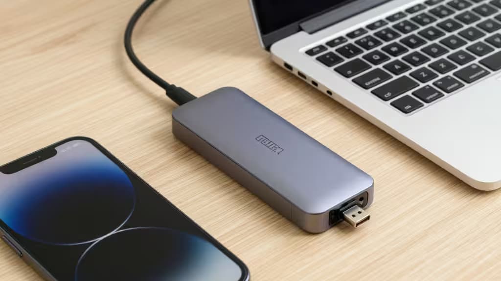 Sleek gray USB-C hub connects laptop and phone on light wood desk.