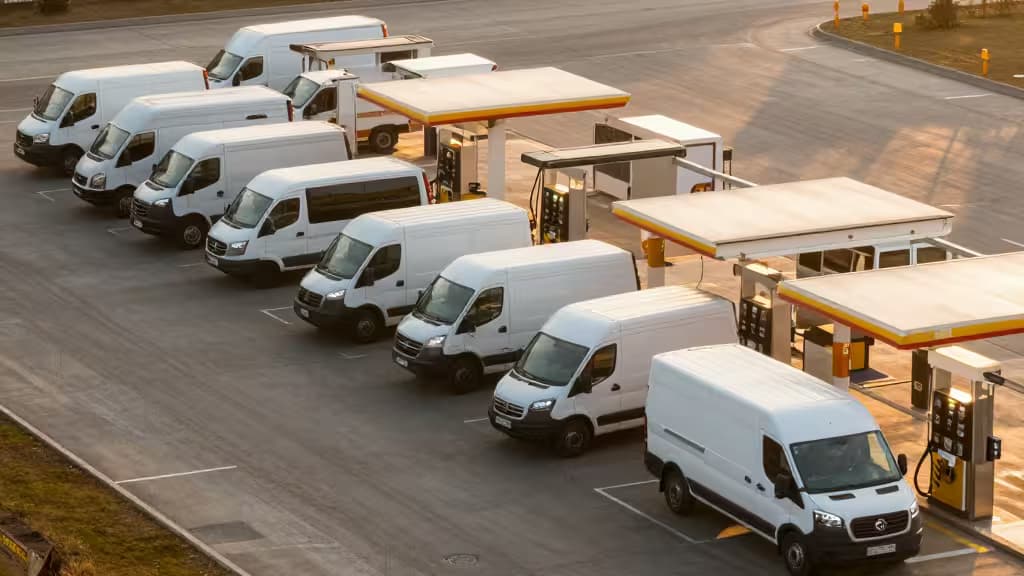 Witte bestelbussen rijden aan bij brandstofpompen onder gele overkappingen, illustrerend efficiënte fleet-tankbeurten voor kleinbedrijf.