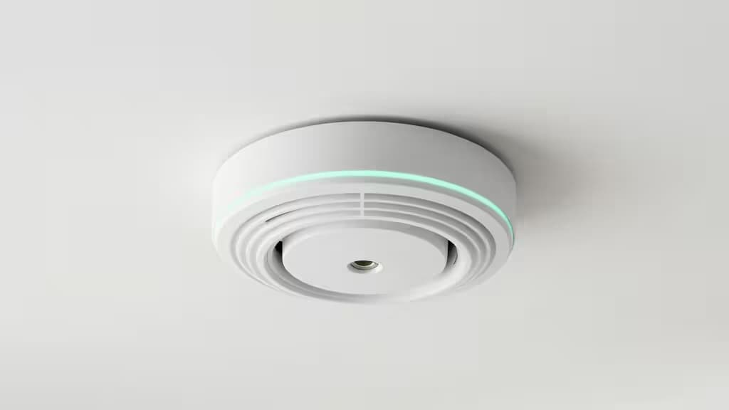 Белый пластиковый детектор дыма со светящимся зелёным LED-кольцом, установленный на белом потолке.