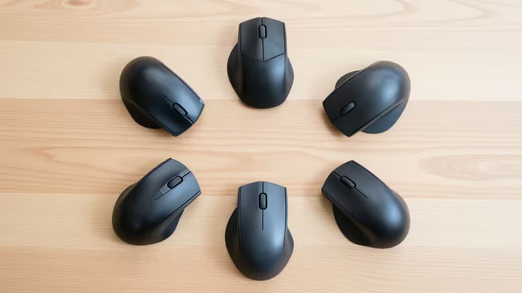 Zes zwarte ergonomische muizen in een cirkel op een lichte houten tafel.