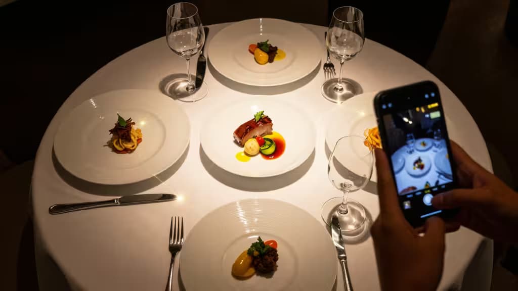 Hands capture gourmet dishes on a white tablecloth using a smartphone, illustrating AI-powered food photography for hospitality marketing.