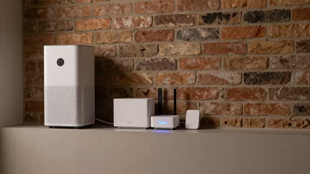 Purificador de aire blanco y dispositivos inteligentes sobre una estantería frente a una pared de ladrillo visto en un sótano moderno y seco.