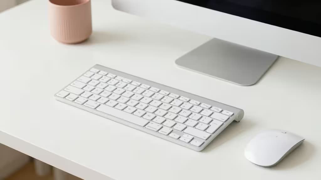Weiße Wireless-Tastatur und Maus auf einem minimalistischen Schreibtisch neben einer rosa Tasse bei natürlichem Licht