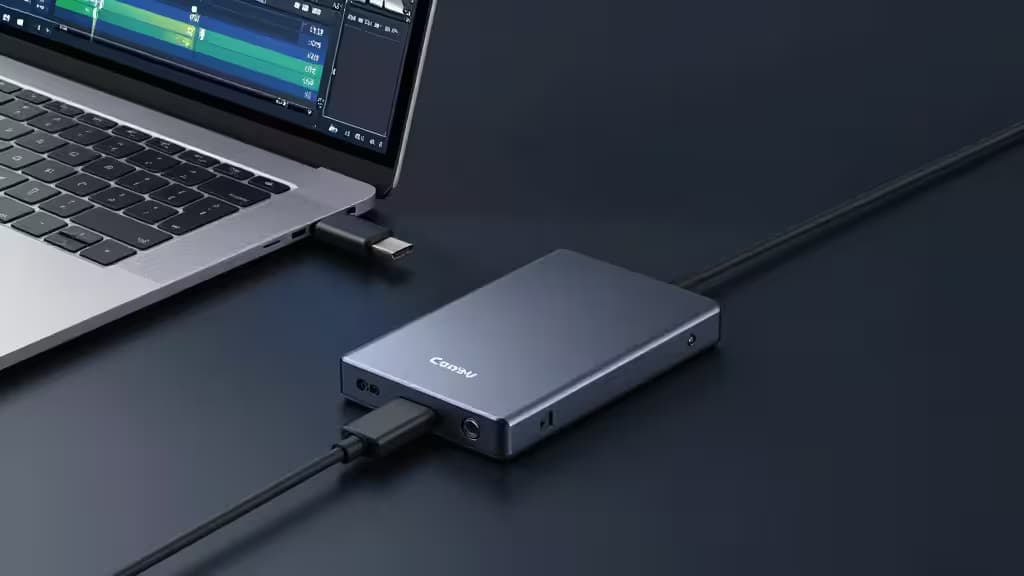 Disque SSD portable posé sur un bureau sombre à côté d'un ordinateur portable affichant une timeline de montage vidéo, câble USB-C branché, éclairage cinématique doux.