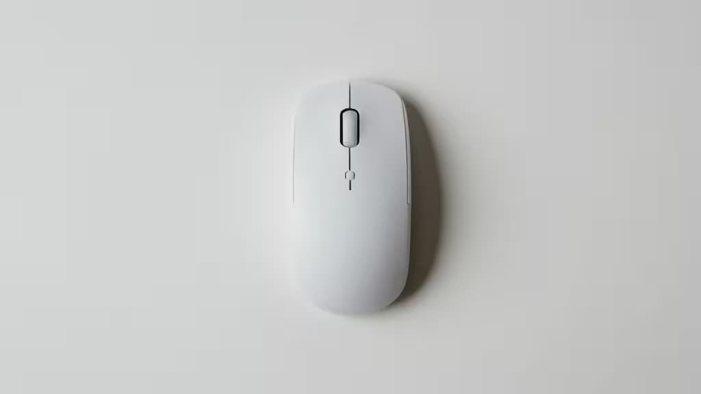 A sleek white wireless mouse rests centered on a minimalist white desk surface, casting a soft shadow.