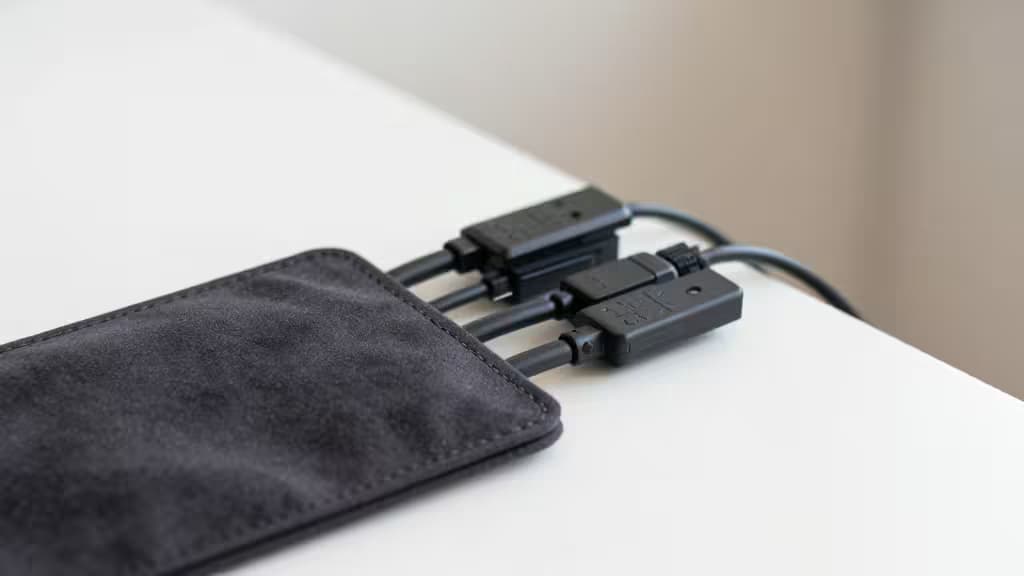 Black fabric sleeve neatly bundles three cables on a white desk surface.