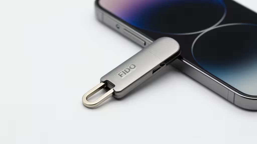 Een geborstelde aluminium FIDO-sleutel met lus ligt naast een iPhone met donker scherm.