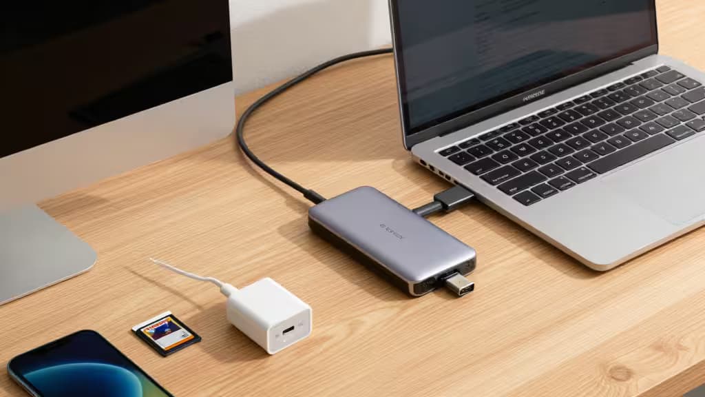 Silver USB-C hub connects MacBook Air to peripherals on light wood desk.