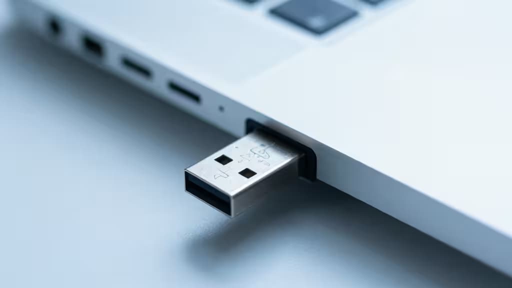 A USB-C security key inserted into a laptop port, photographed in soft blue light with a shallow depth of field.