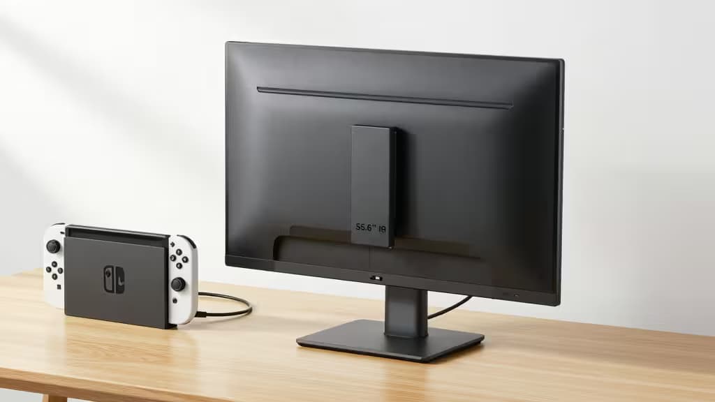 Black 15.6-inch portable monitor stands beside a Nintendo Switch docked on a light wood desk, connected via USB-C cable.