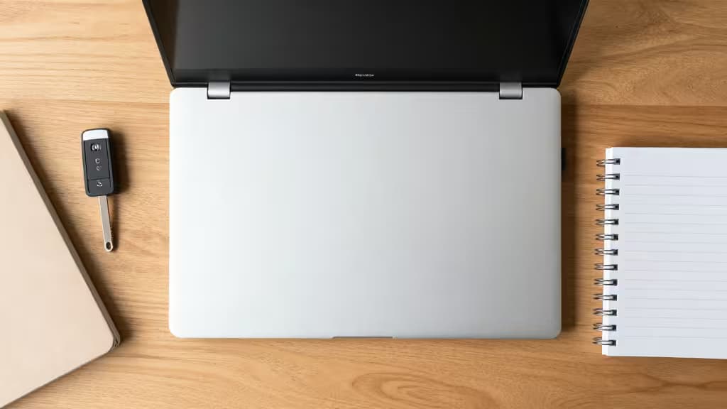 Silver Chromebook rests on wood desk beside notebook and car key fob.