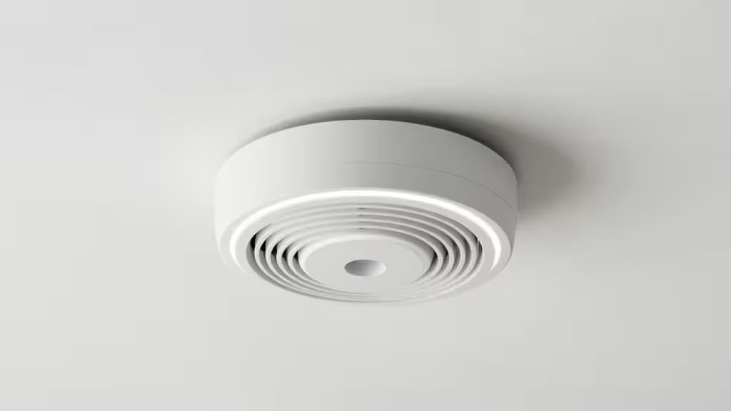 White plastic smoke detector with concentric vents mounts centrally on a smooth, matte white ceiling.