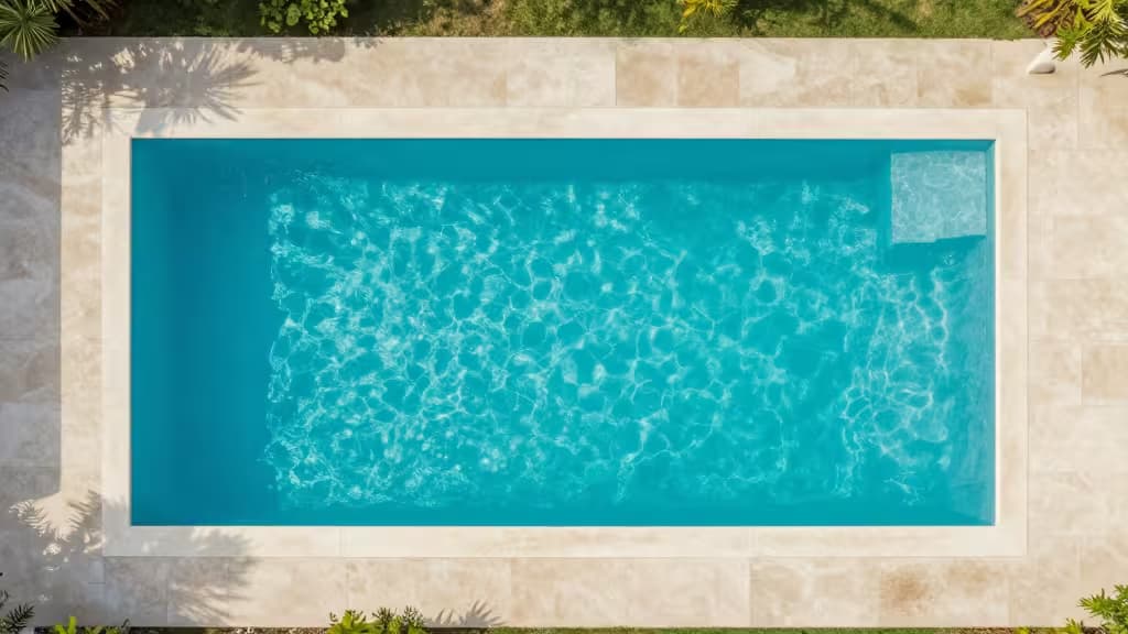 Aerial view of a clear turquoise backyard swimming pool surrounded by modern landscaping in soft morning light
