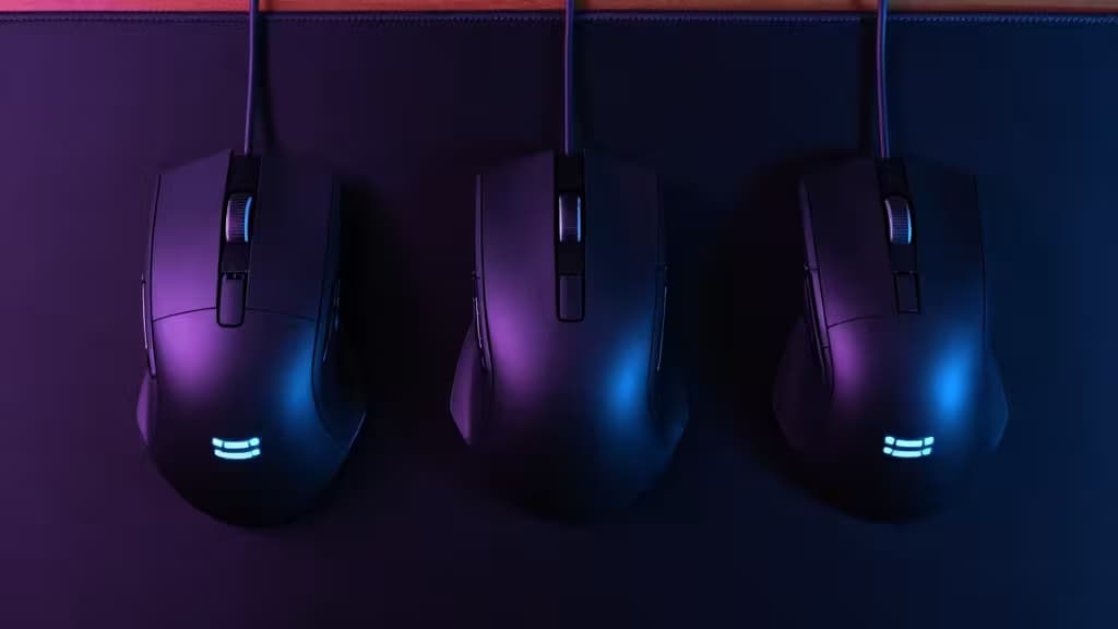 Three sleek gaming mice with RGB lighting rest on a dark desk mat, showcasing ergonomic designs for MMOs.