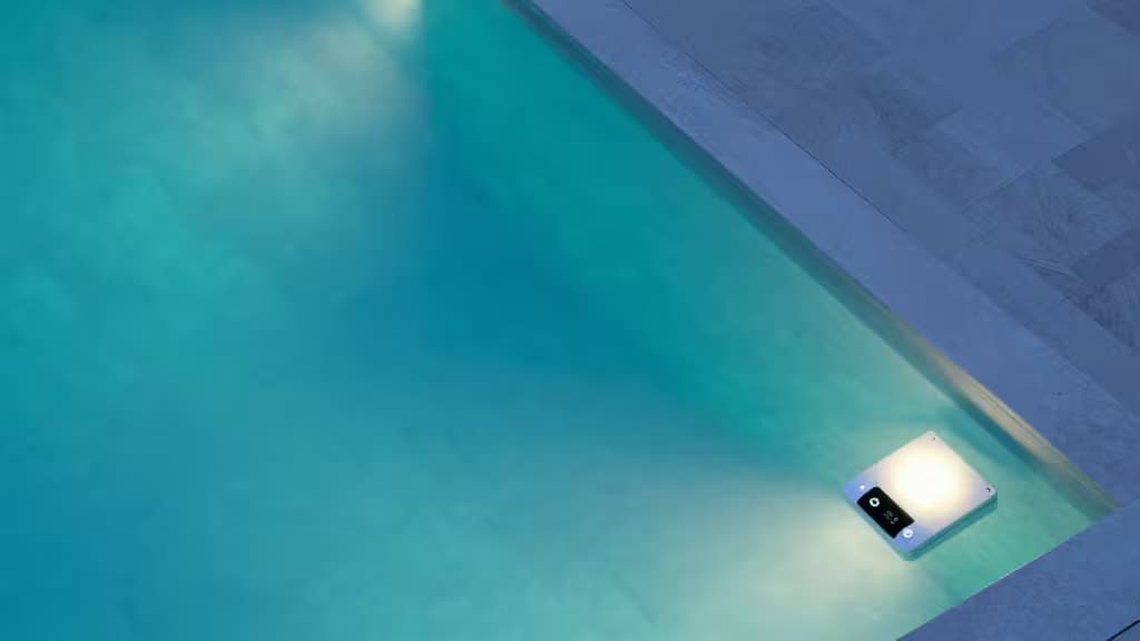 A glowing smart pool light illuminates turquoise water beside a sleek, modern pool deck.