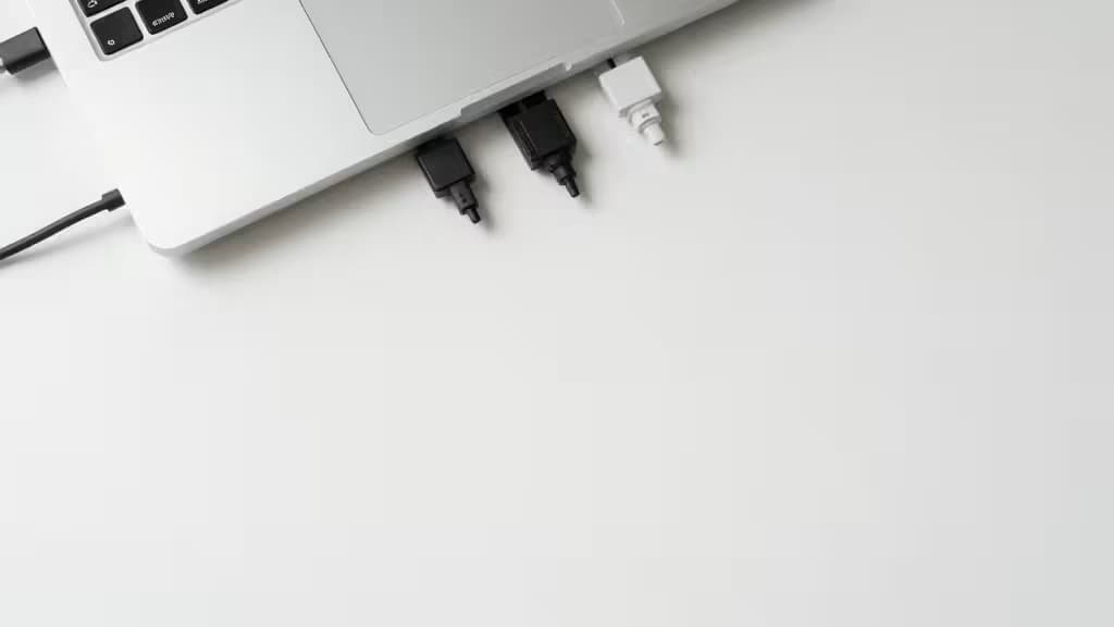 Mesa de escritório minimalista com laptop prateado e cabos organizados sobre superfície branca limpa.