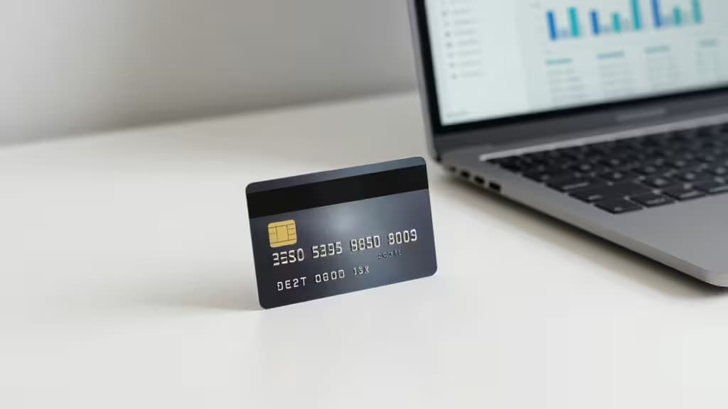 Une carte de débit business noire posée sur un bureau blanc à côté d'un ordinateur portable affichant des graphiques financiers, symbolisant les solutions fintech modernes pour la banque des LLC.