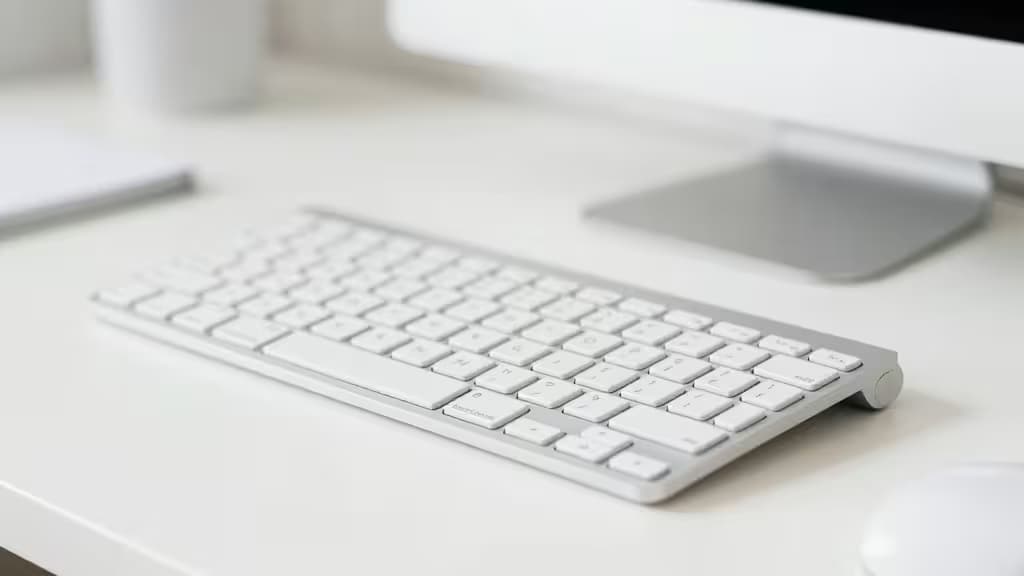 Tastiera wireless bianca su una scrivania minimalista accanto a un monitor, illuminazione naturale soffusa
