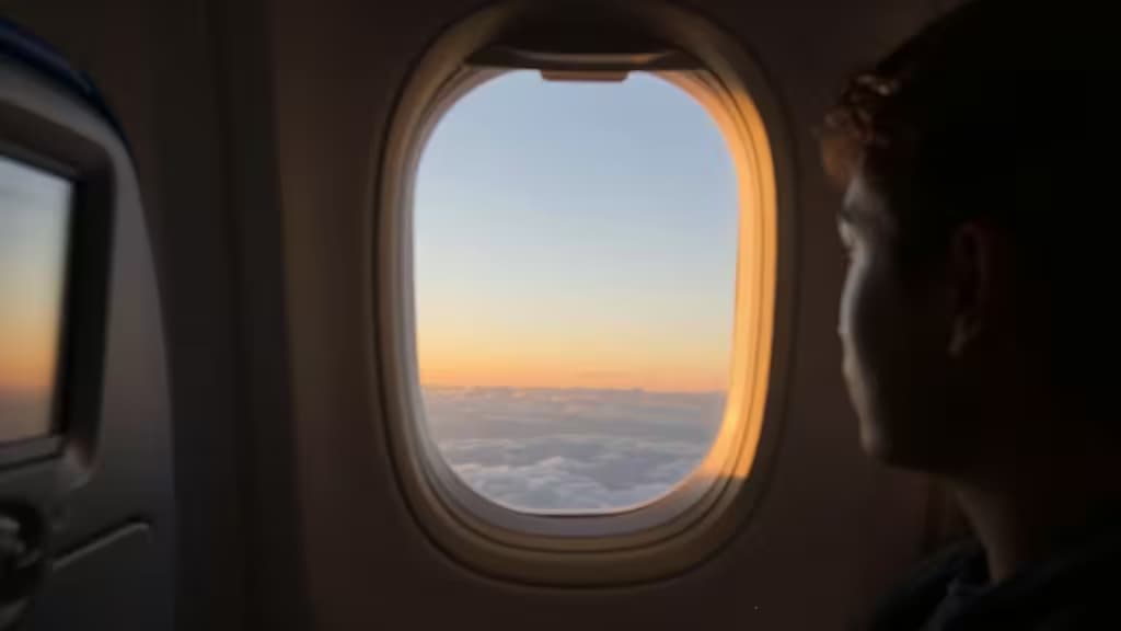 Soft golden light streaming through an airplane cabin window at dusk, with a blurred passenger seat silhouette in the foreground.