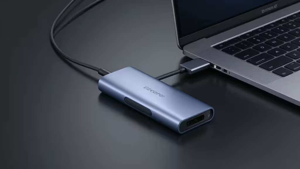 A sleek aluminum USB-C hub connected to a modern laptop on a minimalist desk with soft studio lighting.