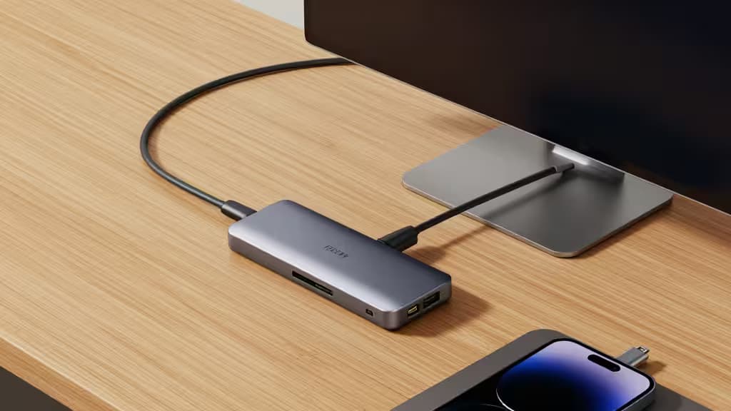 Srebrny hub USB-C łączy iPada Pro z monitorem na drewnianym biurku.